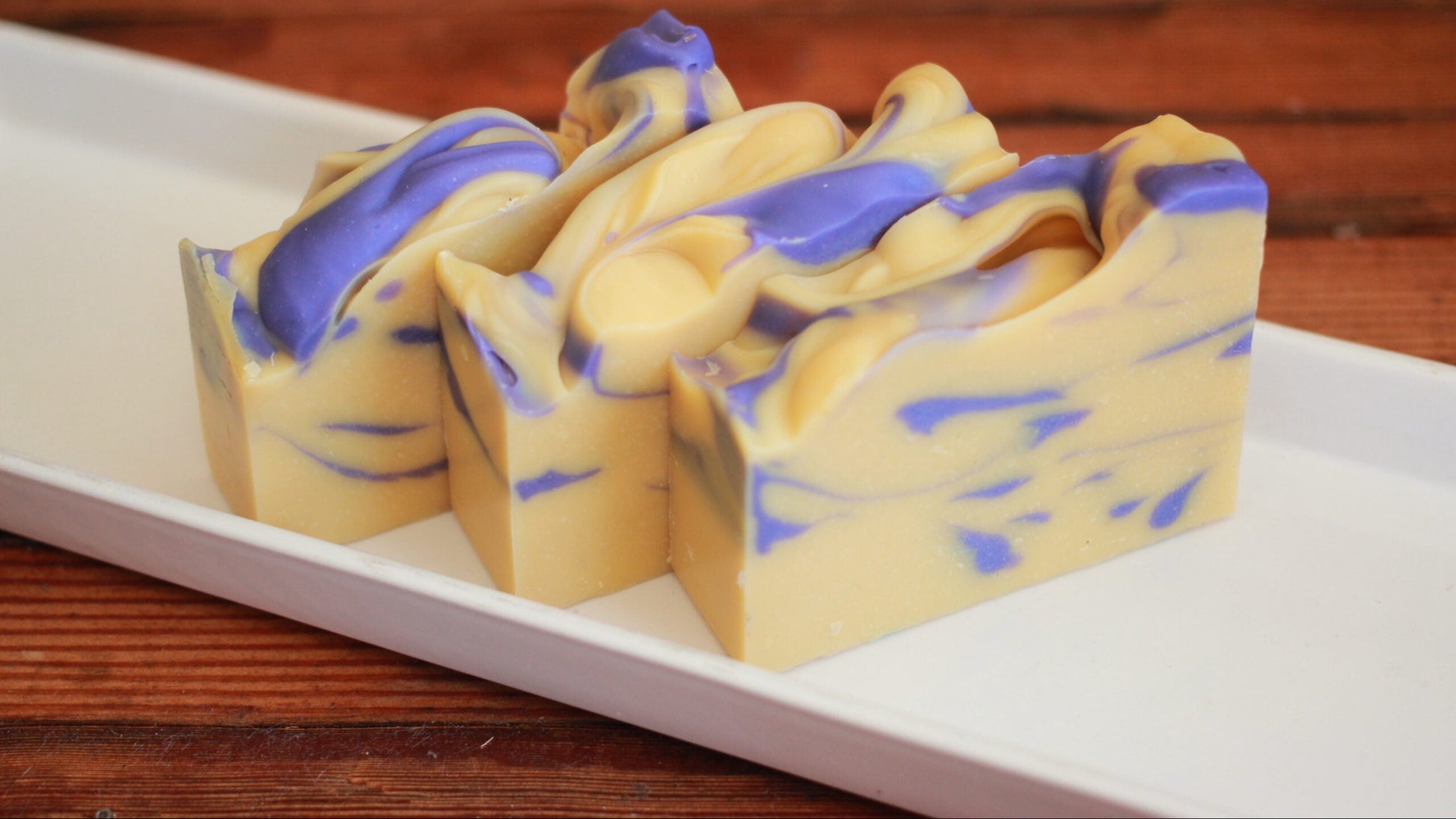 Swirled yellow and blue soap bar on a white plate with a wooden background